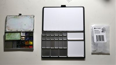 A photograph of a small and well-used paint palette box on the left, a larger palette box in the middle, and a small wax envelope on the right.