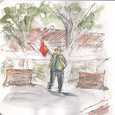 A line and wash sketch of a person standing between two hay bales at a street corner. They are wearing a bright green vest and are raising a red flag with their right arm. 